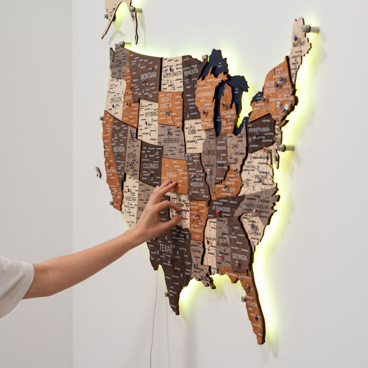 Wooden 3D LED USA map with warm yellow LED edge glow and hand pressing a switch