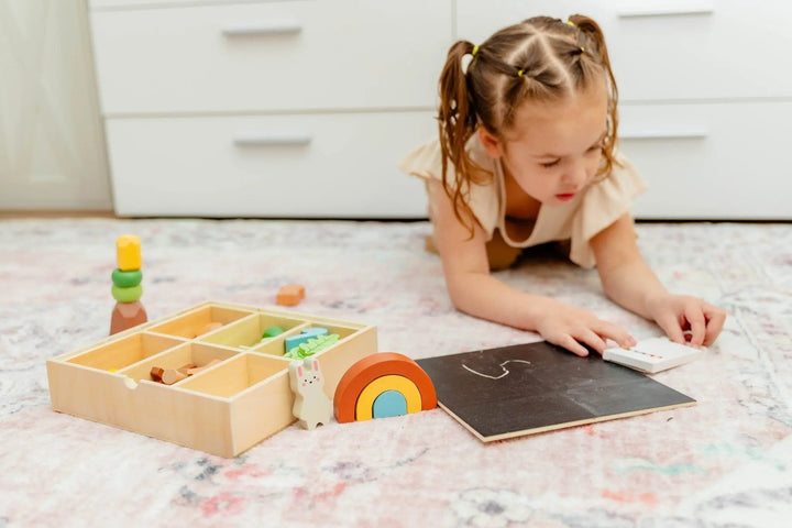 Wooden forest sensory bin with chalkboard and wooden pieces set on floor