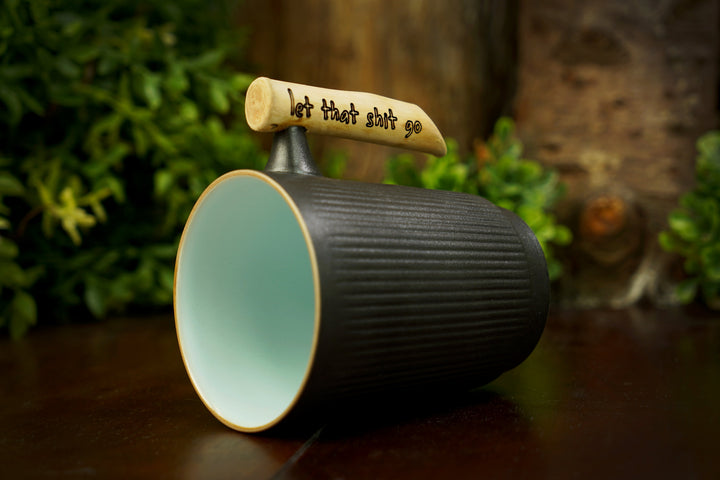 Tilted dark ceramic mug with mint interior and light wood handle with etched text