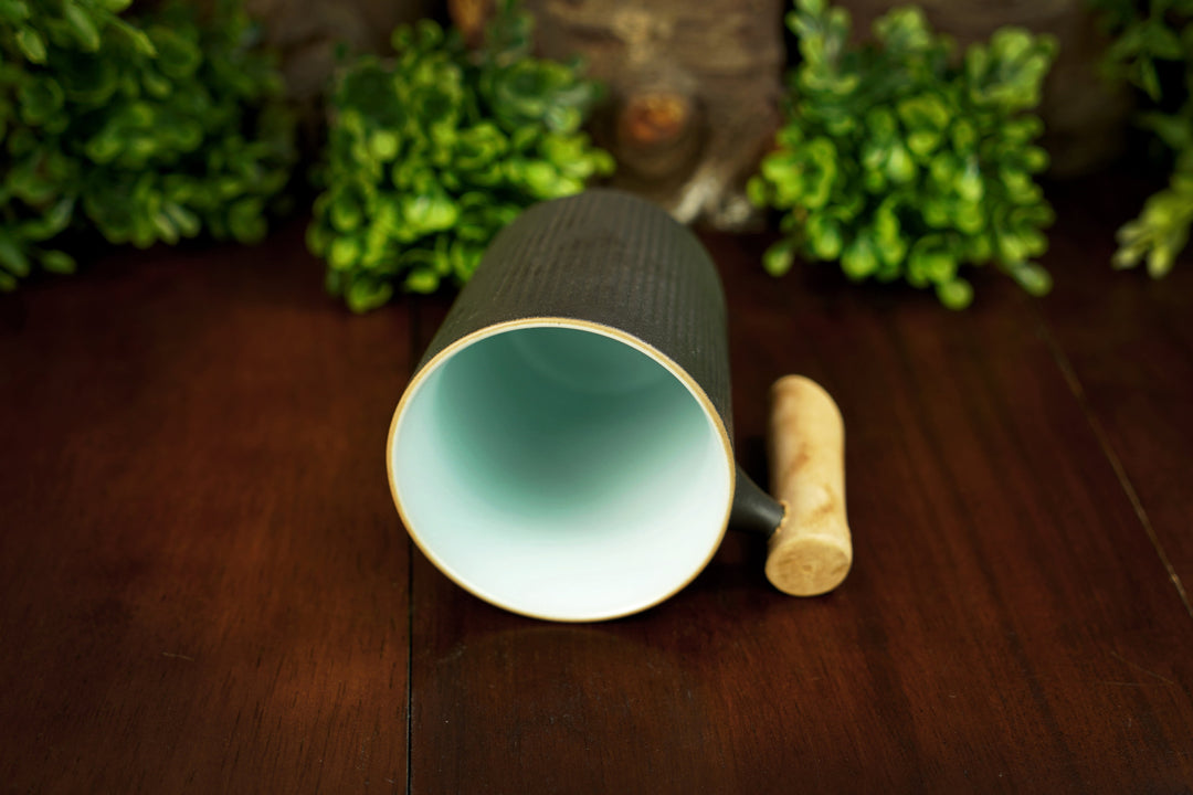 Open-top dark ceramic mug showing mint-green interior and light wood handle