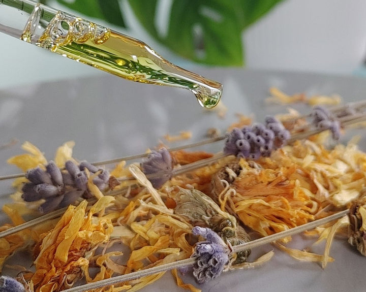 Face oil dropper pouring golden oil over dried flowers and stems